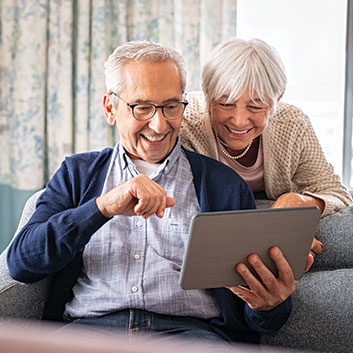 Older couple sitting on couch reading information on a tablet. Read about Gifts That Protect Your Assets Older couple sitting on couch reading information on a tablet. Read about Gifts That Protect Your Assets